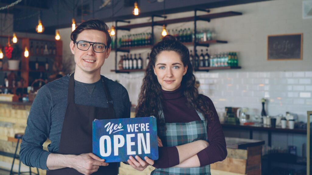 Dueños de un restaurante sonriendo con un cartel de abierto